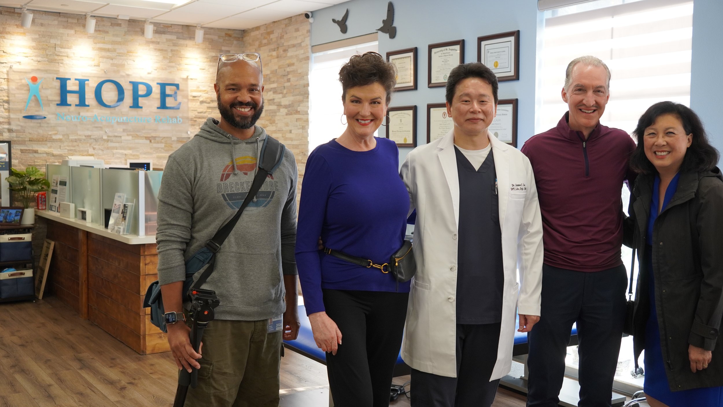 Dr. Lu with visitors and photographer posing in HOPE Clinic lobby near certificates