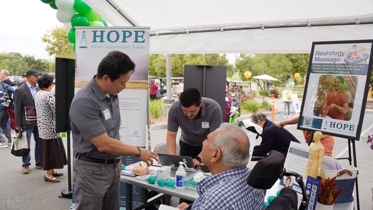Dr. Lu standing at HOPE Clinic neurology massage display at community event