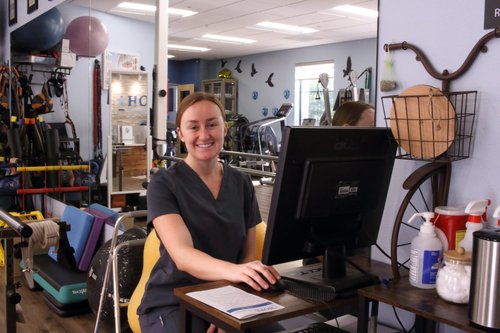 Physical therapy staff member smiling at computer workstation in rehab gym