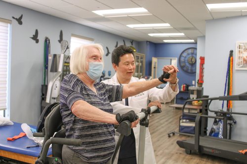 Dr. Lu guiding patient through arm strengthening exercise on standing frame