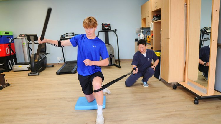 Young athlete performing balance and resistance training on foam pad with Dr. Lu supervising