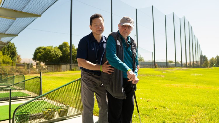 Dr. Lu supporting stroke recovery patient at outdoor golf driving range