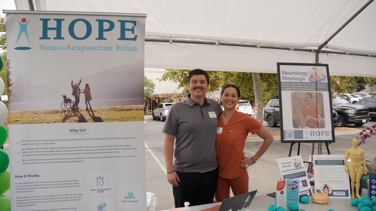 HOPE Clinic therapist and massage therapist at community event booth with neurology massage display